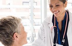 Foto de uma médica sorrindo  com uma paciente no leito de hospital